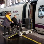 Persona en silla de ruedas accediendo a tren por rampa y con ayuda de un asistente